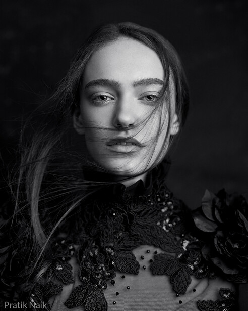 Black and white portrait of a woman with long dark hair and dramatic beaded embellishment on her garment.