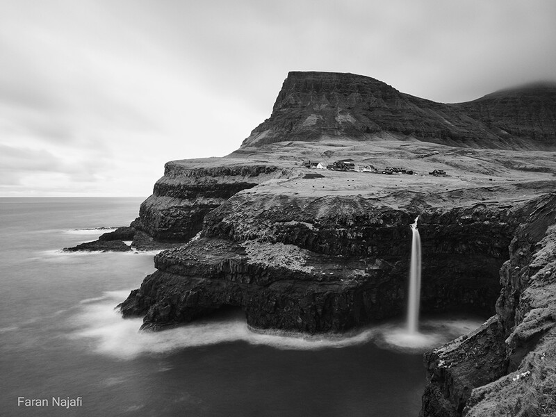 Waterfall cascading from coastal cliffs into the ocean below, captured in black and white.