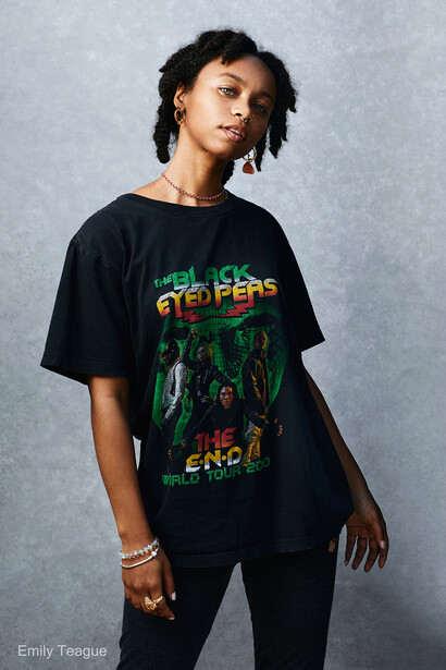 Person wearing vintage band graphic t-shirt styled with layered jewelry against neutral backdrop.