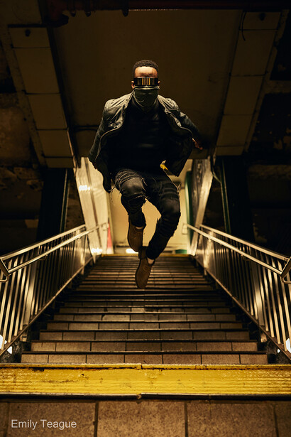 Runner descending concrete stairs at night, illuminated by warm overhead lighting and yellow safety rail.