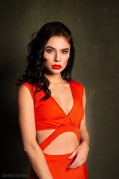 Woman in red wrapped crop top and high-waisted skirt against neutral backdrop.