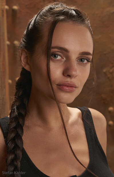 Woman with braided hair against warm brown background, direct gaze toward camera.