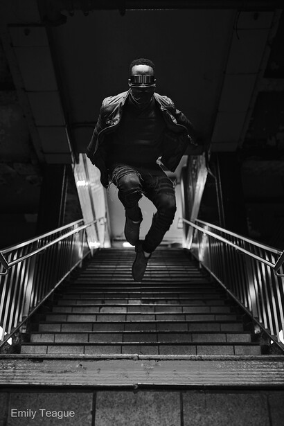 Man running down concrete stairs in monochromatic lighting with dramatic shadows.