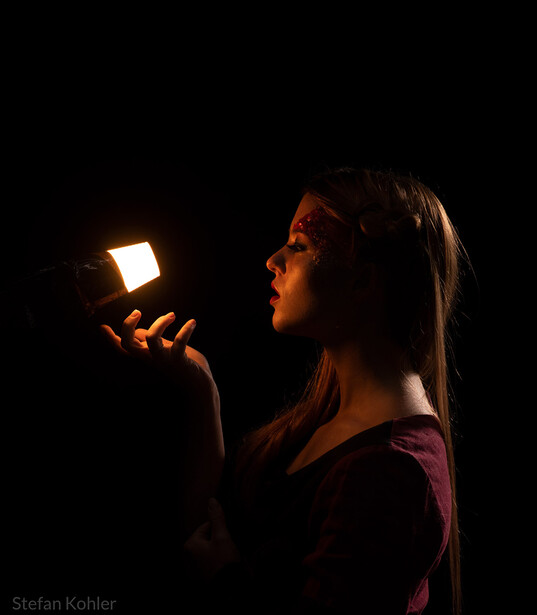 Woman holding a glowing LED light panel against a dark background, illuminating her face with warm amber light.