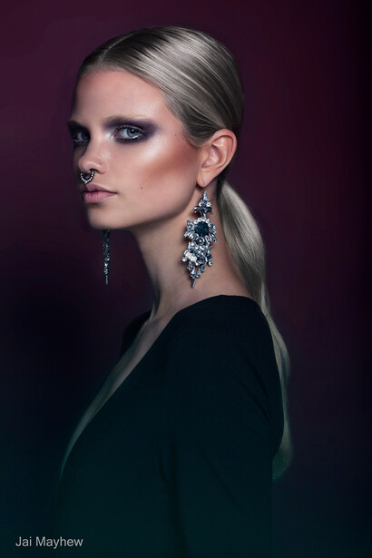 Portrait of a woman with blonde hair and statement earrings against a dark purple background.