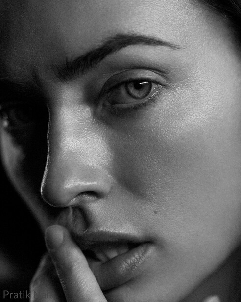 Black and white portrait of a woman's face in profile, hand near mouth, dramatic side lighting.