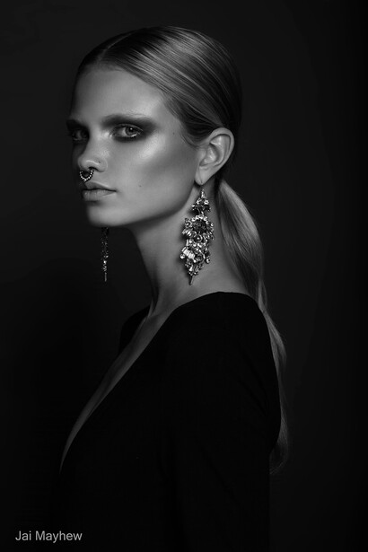 Portrait of a woman with slicked-back blonde hair wearing statement chandelier earrings against a dark background.