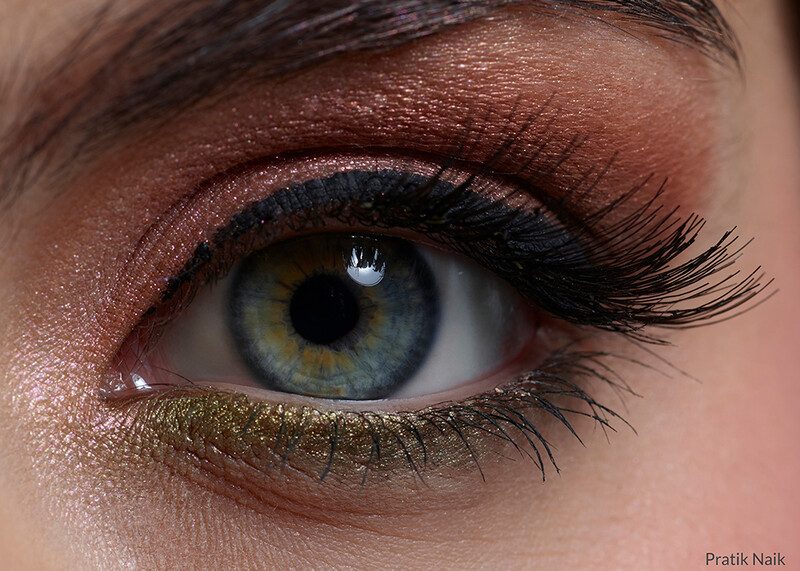 Close-up of a blue-green eye with warm brown eyeshadow, black winged eyeliner, and gold lower lash line detail.