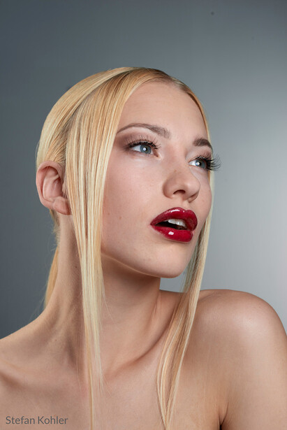 Woman with platinum blonde hair and red lipstick against neutral gray background.