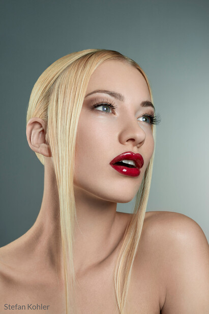 Woman with platinum blonde hair and bold red lipstick against a neutral blue-gray background.