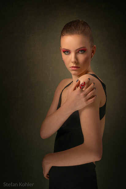 Woman in black sleeveless top with hand on shoulder against dark gradient background.