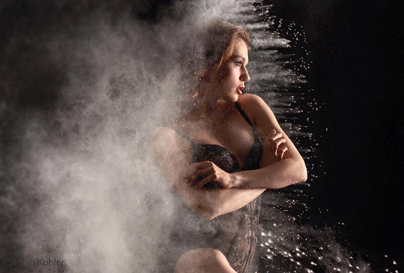 Woman in profile surrounded by swirling powder and water droplets against a dark background.