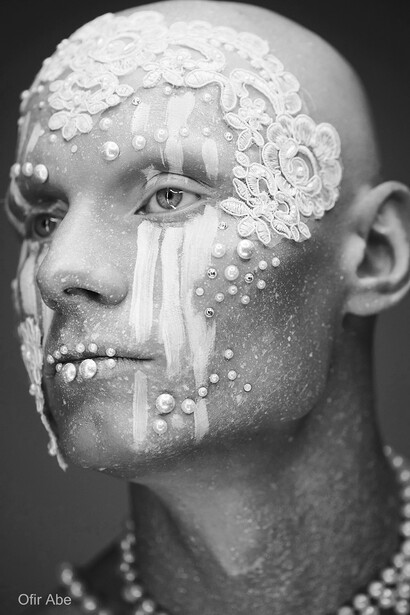 Man's face in profile with white textured material and spherical beads applied to half of face.