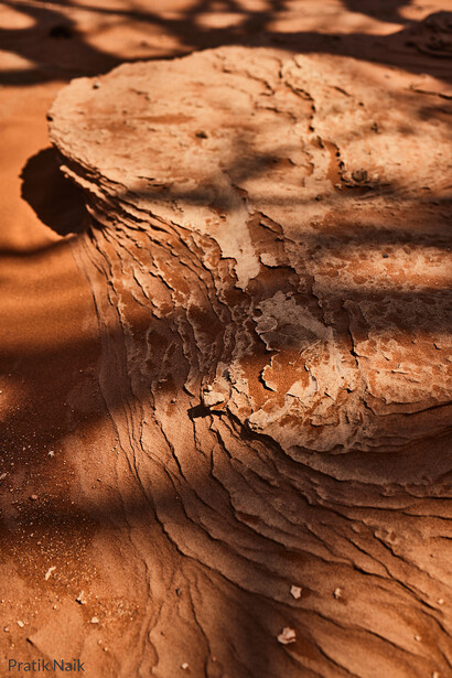 Close-up of layered rock formations with sharp shadows cast across tan and rust-colored stratified surfaces.