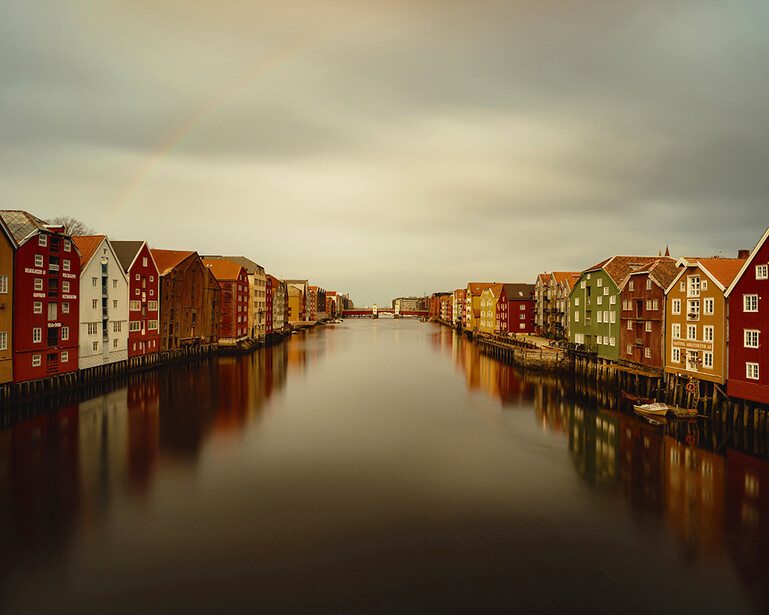Colorful waterfront buildings reflected in still water under overcast sky.