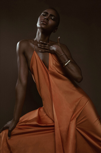 Woman in orange draped fabric against dark background, looking upward with contemplative expression.