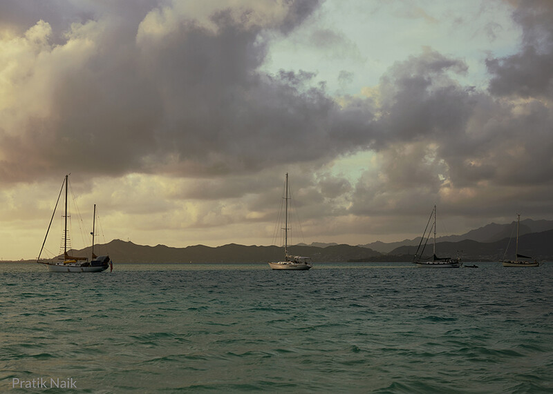Sailboats anchored in calm tropical waters beneath dramatic cloud-filled sky.