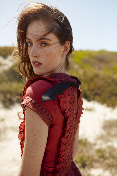Woman in burgundy textured dress looking over shoulder in desert landscape.