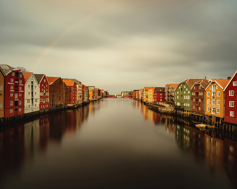 Colorful historic buildings line both sides of a still canal under overcast sky.
