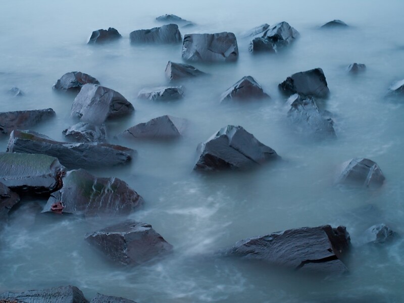 Rocky coastal rocks partially submerged in misty, flowing water with long exposure effect.