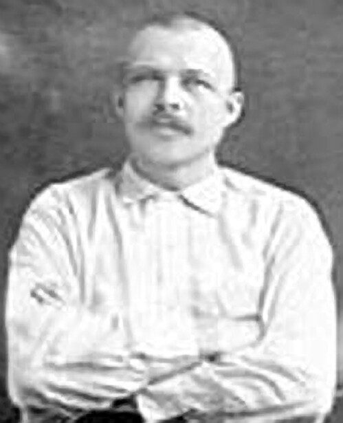 Black and white portrait photograph of a man with a mustache wearing a light-colored collared shirt.