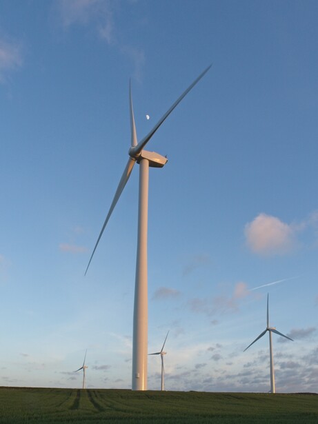 Modern wind turbine with two blades against blue sky and green field, with additional turbines visible in the distance.