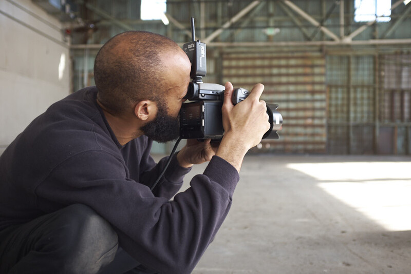 Photographer crouching while composing a shot with a film camera in an industrial warehouse space.