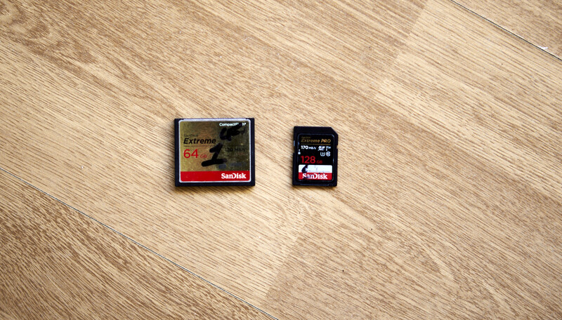 Two memory cards on a light wood surface: a larger SanDisk Extreme CompactFlash card and a smaller SDXC card.