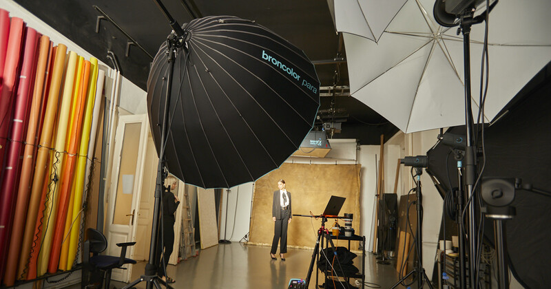 Professional studio setup with large parabolic umbrella, softbox, and reflector panels around a central shooting area.