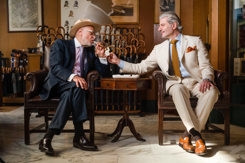 Two men in business attire seated in leather chairs, engaged in conversation in a wood-paneled interior.