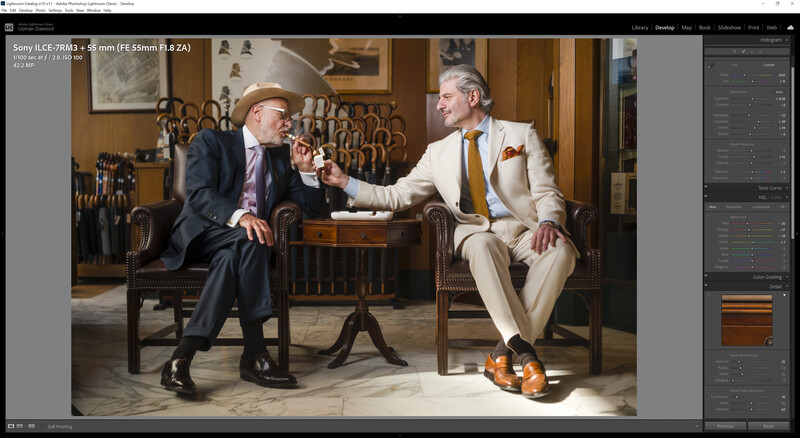 Two men in suits sit facing each other in a wood-paneled room, gesturing in conversation.
