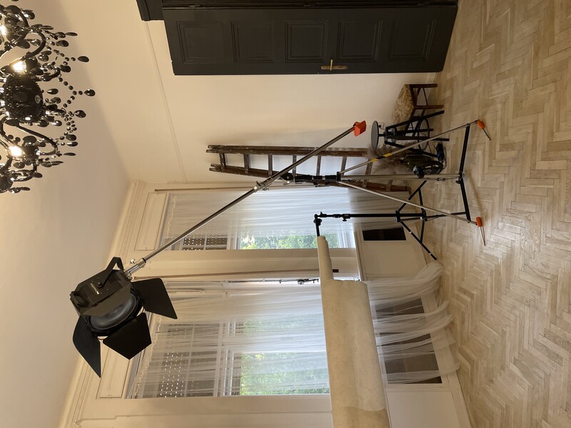 Professional film lighting setup with large soft-box fixture on tripod in residential room.