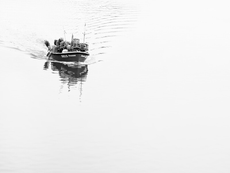 Small fishing boat creating ripples across calm water in minimalist black and white composition.