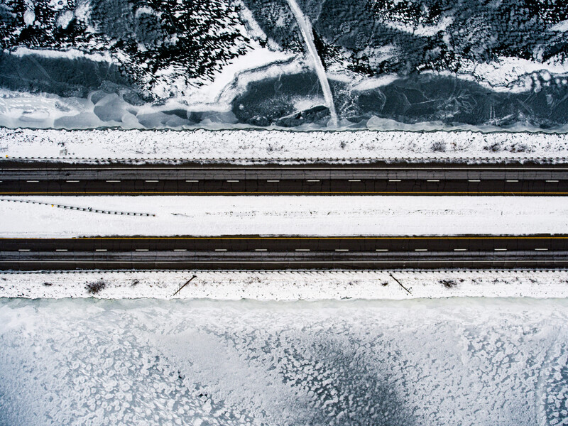 Aerial view of snowy landscape with railroad tracks cutting through white fields and forested areas.