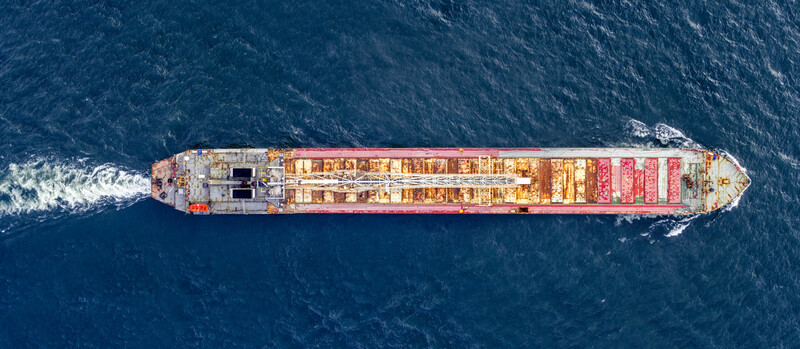 Aerial view of a massive cargo container ship loaded with colorful stacked containers sailing through deep blue ocean waters.
