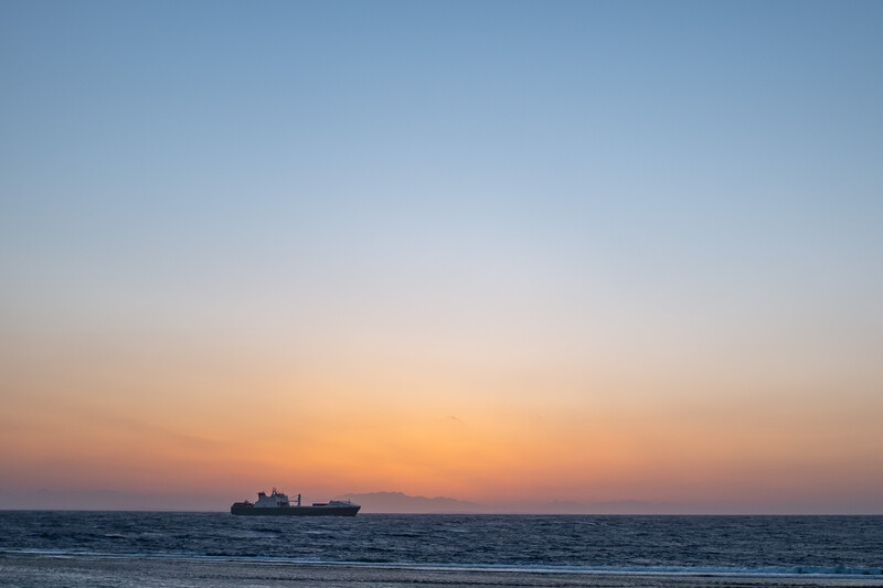 Cargo ship silhouetted against an orange and blue twilight sky on the horizon.