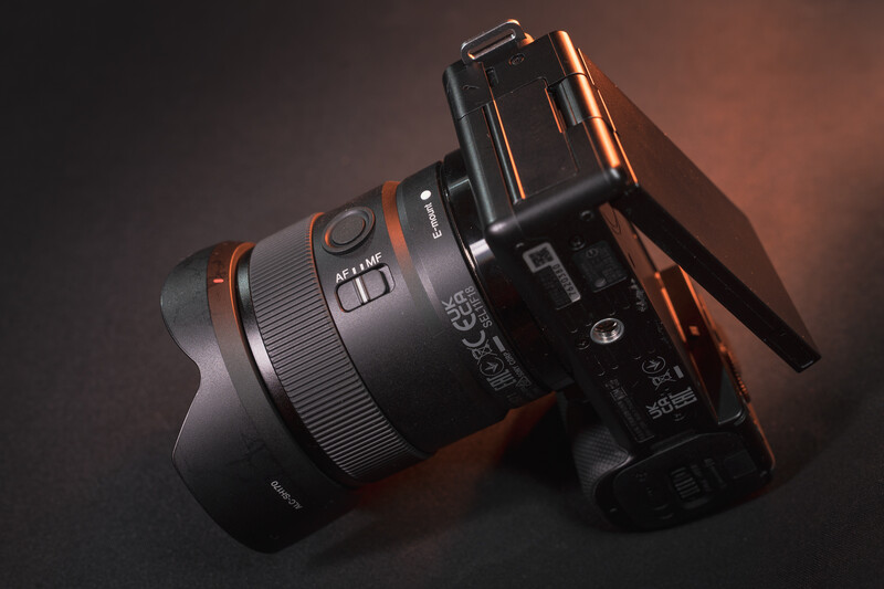 Sony mirrorless camera with attached telephoto lens on dark surface with warm accent lighting.