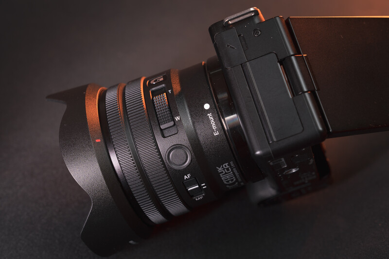 Wide-angle lens with orange and black finish attached to mirrorless camera body against dark background.