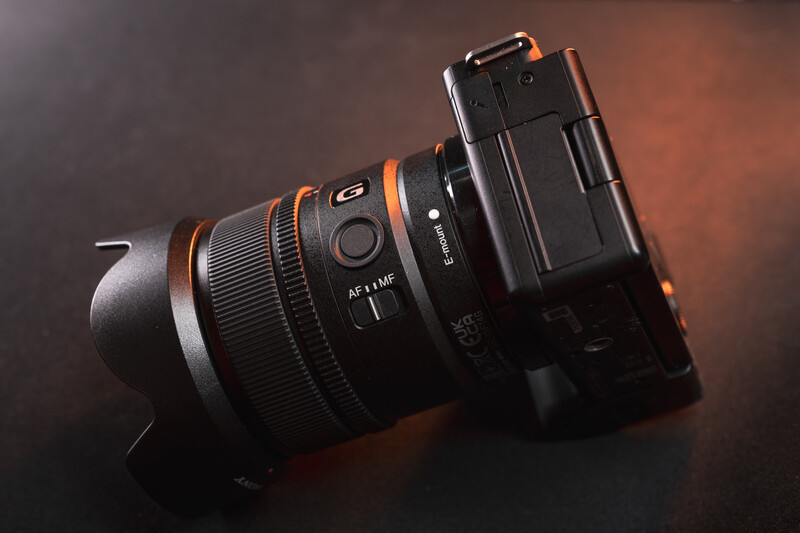 Sony mirrorless camera with attached telephoto lens featuring orange accents on dark surface.