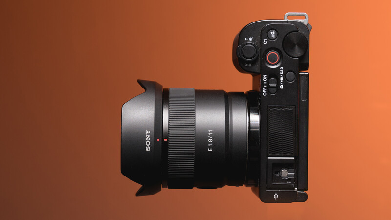 Sony mirrorless camera with wide-angle lens attached, displayed against warm orange background.