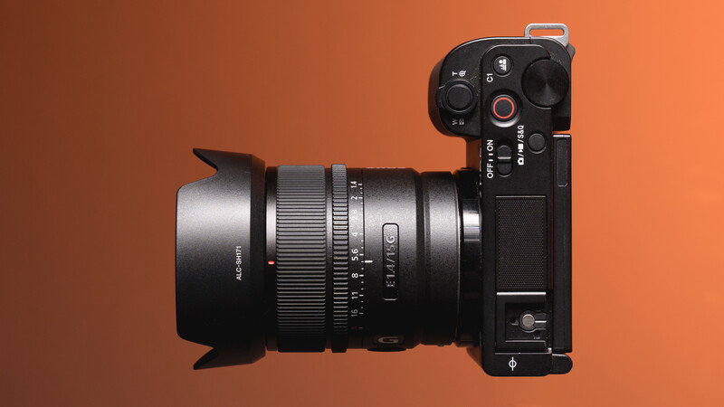 Mirrorless camera with wide-angle lens and lens hood mounted, viewed from above against warm orange background.