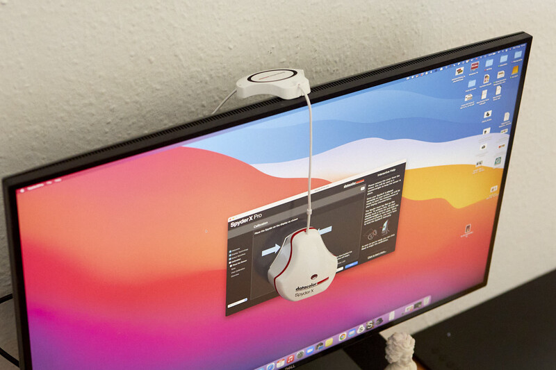 Computer monitor displaying colorful gradient wallpaper with a wireless mouse positioned on top of the screen bezel.