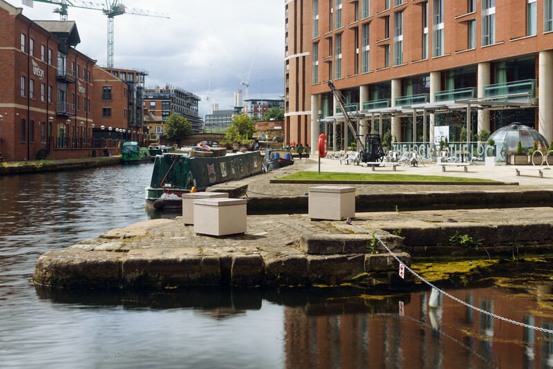 Waterfront plaza with brick buildings, moored narrowboat, and outdoor seating areas along a canal.