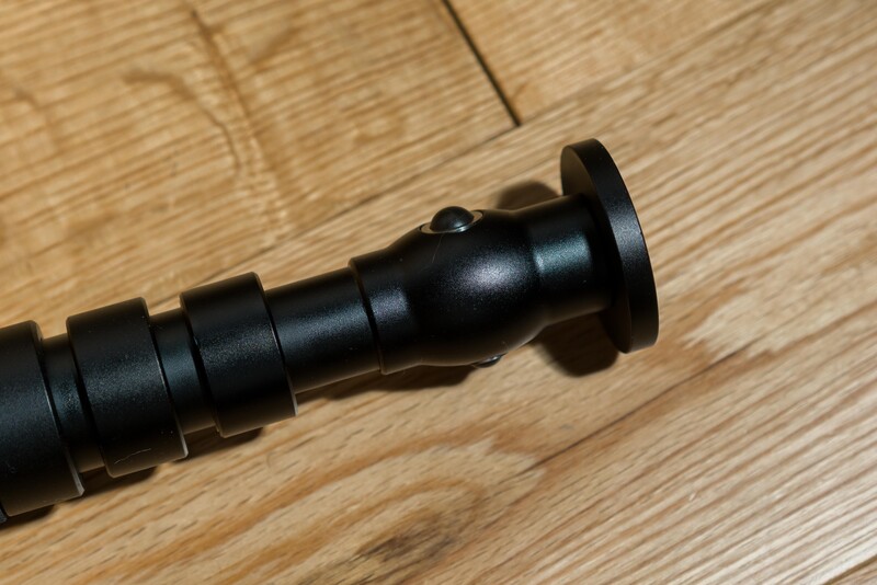 Close-up of a black telephoto lens barrel with threaded segments and a cylindrical lens hood on a wooden surface.