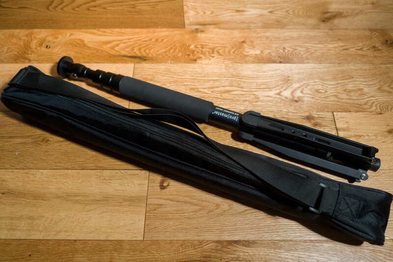 Black camera strap and lens cap laid out on wooden flooring.