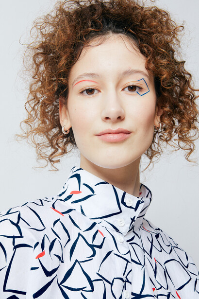 Portrait of a person with curly auburn hair wearing a patterned blue and white shirt against a neutral background.
