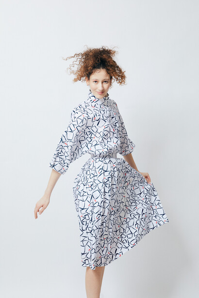 Woman in a patterned blue and white dress poses against a neutral background.