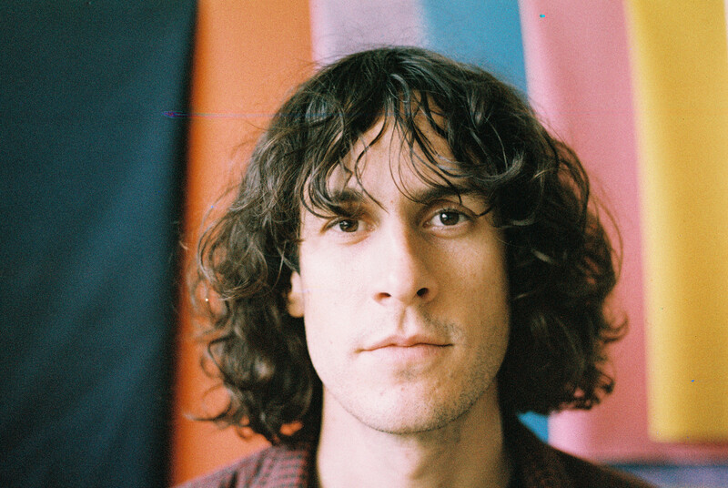 Person with shoulder-length dark wavy hair against a colorful striped background.