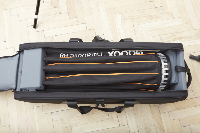 Camera lens with orange and black accents stored in a padded black case with gray interior padding.
