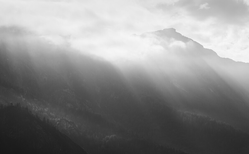 Mountain peak shrouded in mist with dramatic crepuscular rays breaking through clouds.